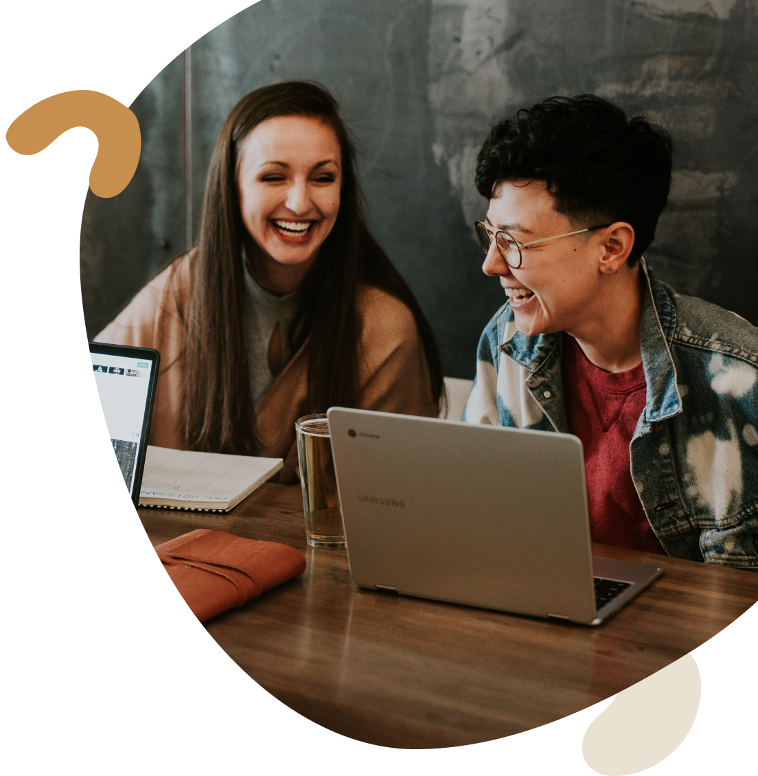 Two young women sit in front of a computer laughing